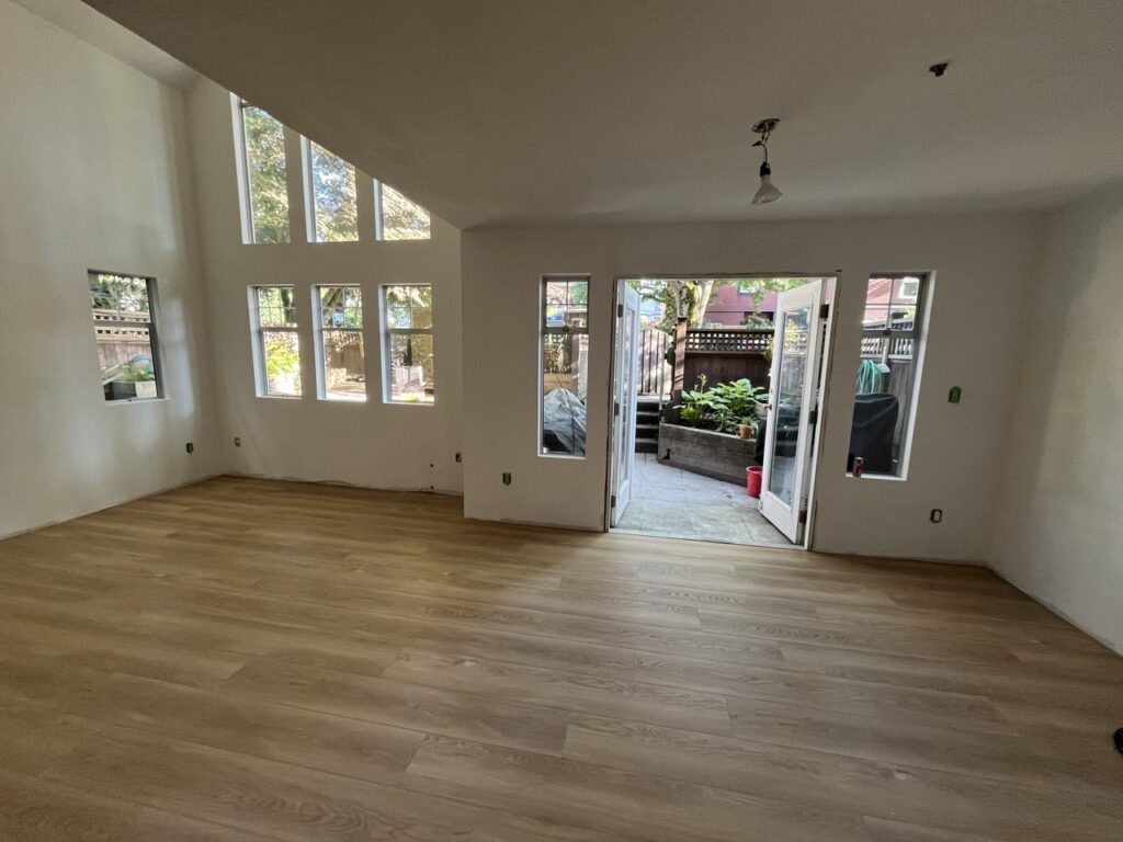 Wide-plank wood-look flooring across an open living room with high windows