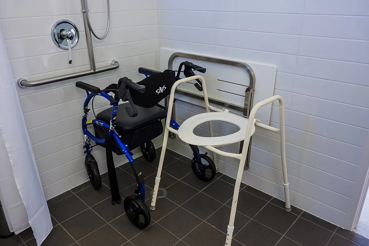 Accessible bathroom with wall-mounted grab bars, a shower chair and a rolling walker