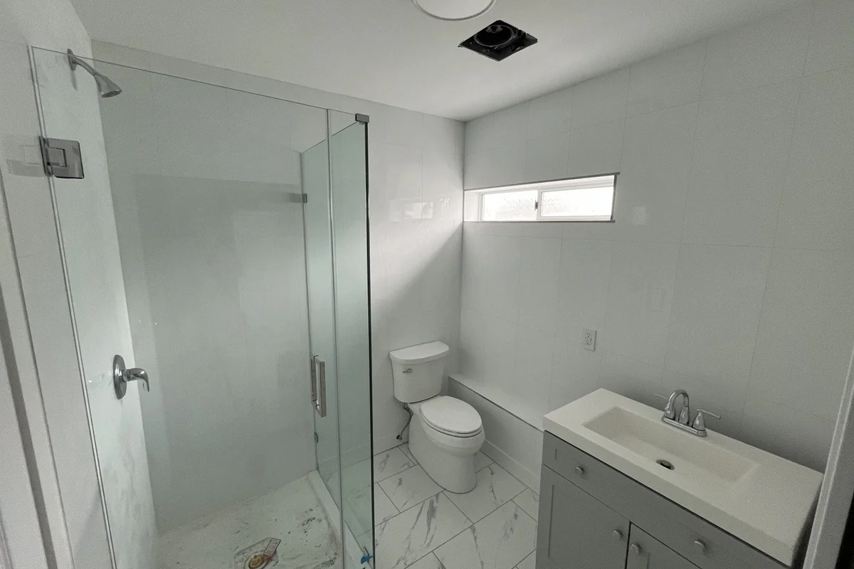 Renovated bathroom with a frameless glass shower, marble-look tile and a new vanity