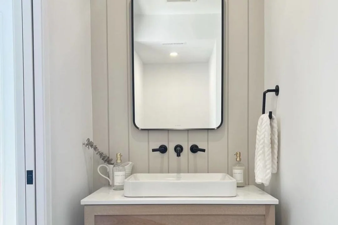 Floating wood vanity with a vessel sink, black wall-mounted faucet and shiplap wall