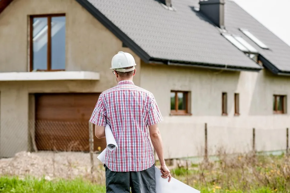 Contractor in a hard hat carrying plans to a home under construction